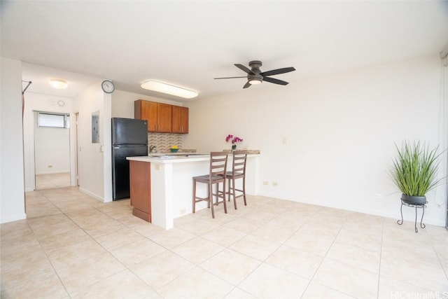 kitchen with light countertops, a ceiling fan, freestanding refrigerator, a kitchen breakfast bar, and brown cabinets