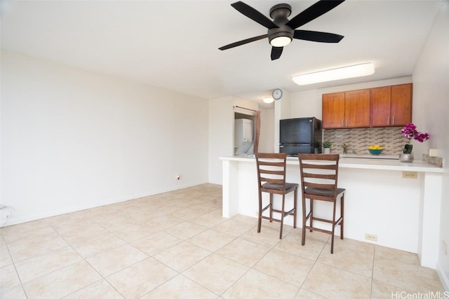 kitchen featuring a kitchen bar, light countertops, tasteful backsplash, freestanding refrigerator, and a peninsula