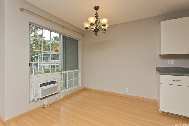 unfurnished dining area featuring light wood-style floors, an AC wall unit, baseboards, and an inviting chandelier