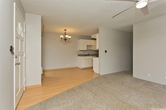 unfurnished living room featuring a textured ceiling, a sink, ceiling fan with notable chandelier, light wood-type flooring, and light colored carpet
