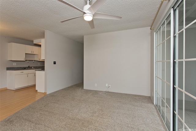 unfurnished living room featuring a ceiling fan, a sink, a textured ceiling, and light colored carpet