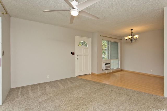 carpeted spare room featuring a wall mounted AC, a textured ceiling, and ceiling fan with notable chandelier