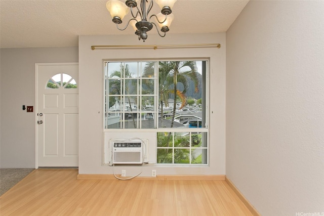 entryway with wood finished floors, a healthy amount of sunlight, a wall unit AC, and a notable chandelier