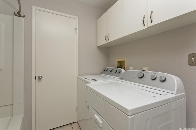 clothes washing area featuring separate washer and dryer, light tile patterned floors, and cabinet space