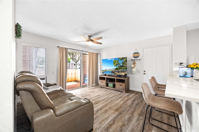 living area with baseboards, a textured ceiling, a ceiling fan, and wood finished floors