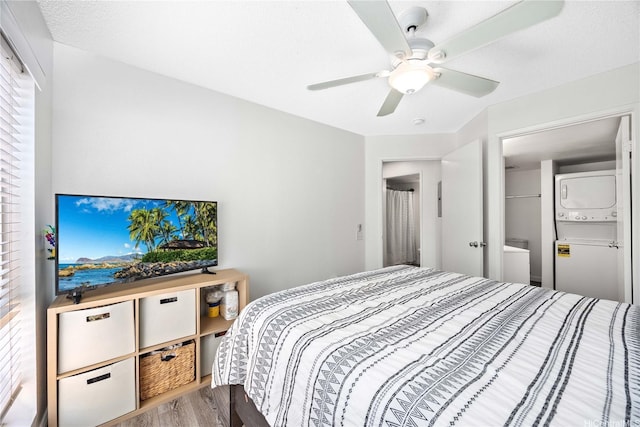 bedroom with wood finished floors, a ceiling fan, and stacked washer / drying machine