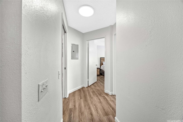 corridor featuring a textured wall, baseboards, and wood finished floors