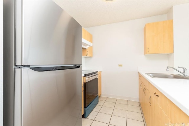 kitchen with light countertops, a sink, freestanding refrigerator, light brown cabinetry, and electric range