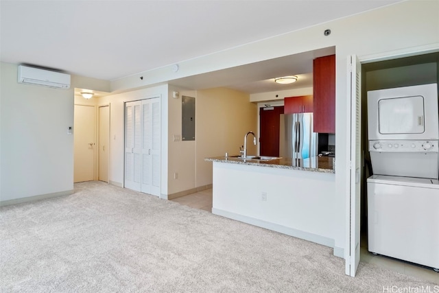 kitchen featuring stacked washer / drying machine, freestanding refrigerator, a sink, a wall unit AC, and light colored carpet