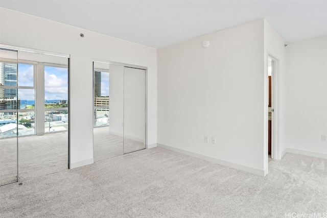 unfurnished bedroom with a city view, baseboards, multiple closets, and carpet flooring