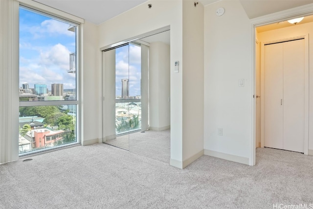 carpeted empty room featuring floor to ceiling windows, baseboards, and a view of city