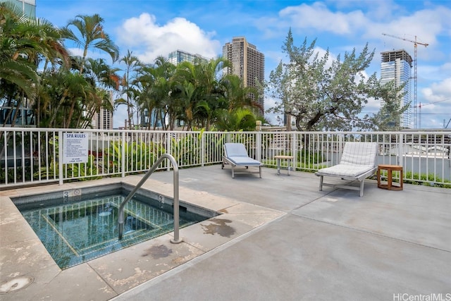 view of pool with a patio area, a view of city, and a hot tub