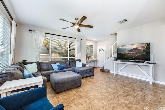 living room featuring baseboards, a ceiling fan, visible vents, and stairway