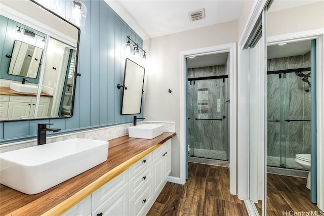 bathroom with a stall shower, wood finished floors, a sink, and visible vents