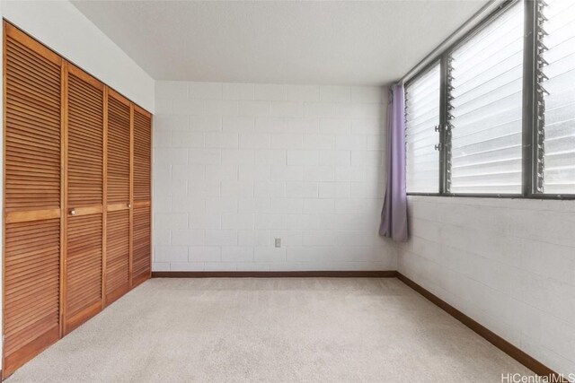 unfurnished bedroom featuring a closet, concrete block wall, and carpet