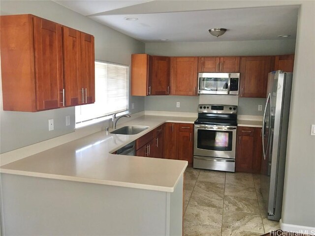 kitchen featuring light countertops, a sink, a peninsula, appliances with stainless steel finishes, and brown cabinetry