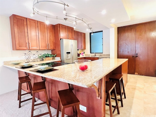 kitchen featuring a kitchen breakfast bar, light stone counters, a sink, a peninsula, and white fridge with ice dispenser