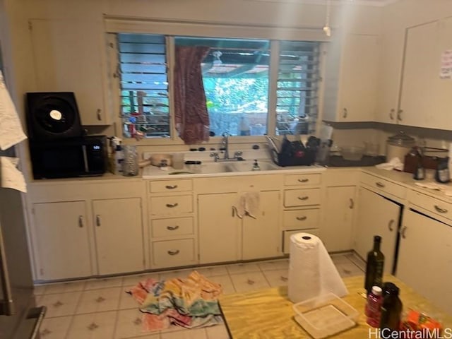 kitchen with light countertops, a sink, black microwave, white cabinetry, and light tile patterned floors