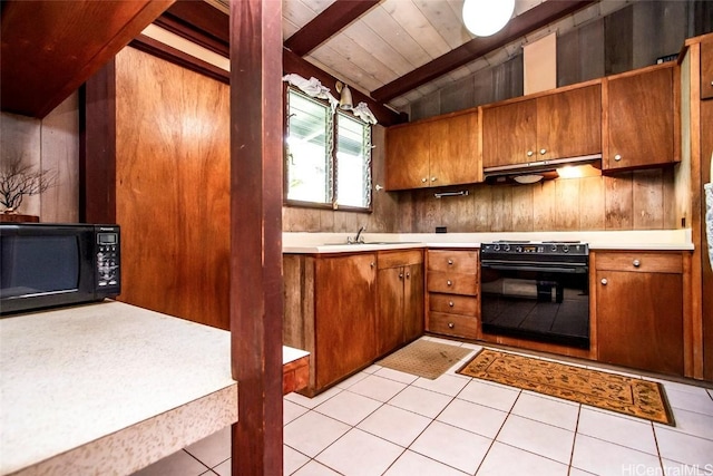 kitchen with light tile patterned floors, lofted ceiling with beams, under cabinet range hood, black appliances, and brown cabinets