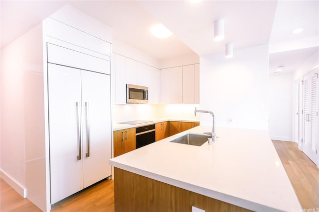 kitchen featuring a sink, stainless steel microwave, light countertops, light wood-style floors, and paneled refrigerator