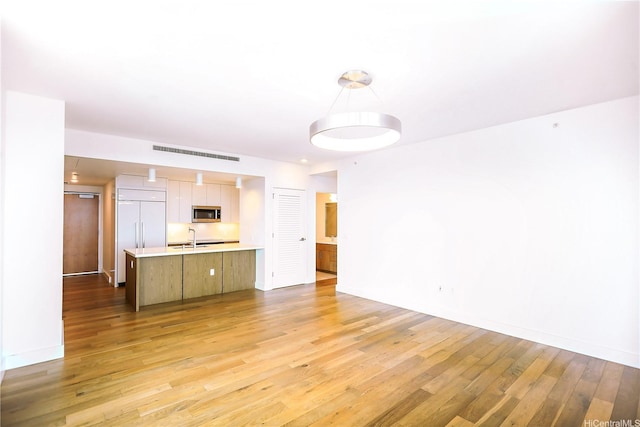 kitchen with visible vents, stainless steel microwave, a sink, light wood-style floors, and light countertops