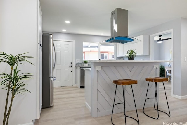 kitchen with light countertops, stainless steel appliances, white cabinetry, island range hood, and a kitchen breakfast bar