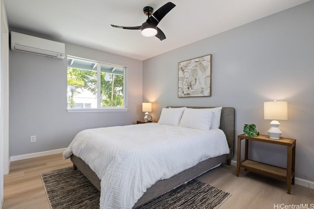 bedroom with a wall mounted AC, baseboards, and light wood finished floors