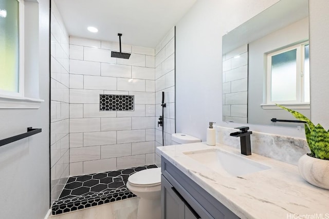 bathroom with toilet, tiled shower, and vanity