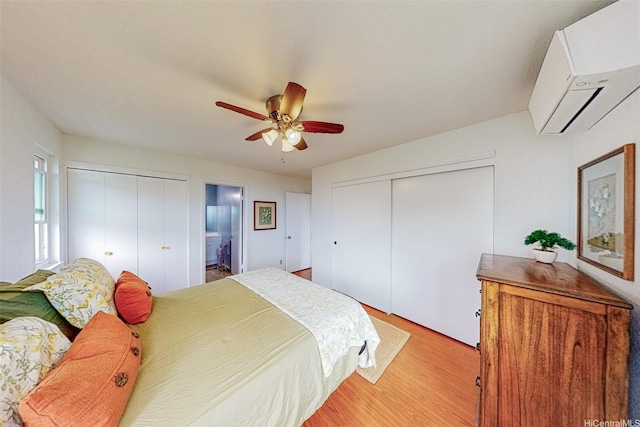 bedroom featuring ceiling fan, a wall mounted AC, ensuite bath, and wood finished floors