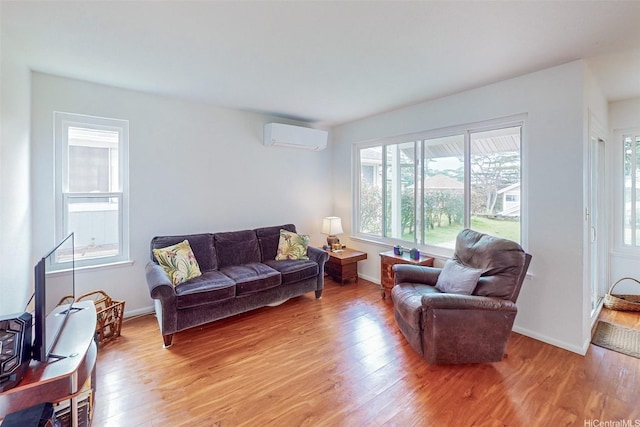 living area featuring a wall mounted air conditioner, baseboards, and light wood-type flooring