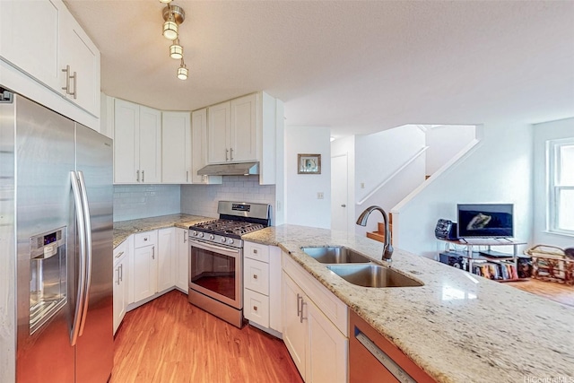 kitchen featuring a sink, stainless steel appliances, light wood-type flooring, under cabinet range hood, and white cabinets