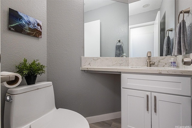 half bathroom with toilet, wood finished floors, vanity, a textured wall, and baseboards