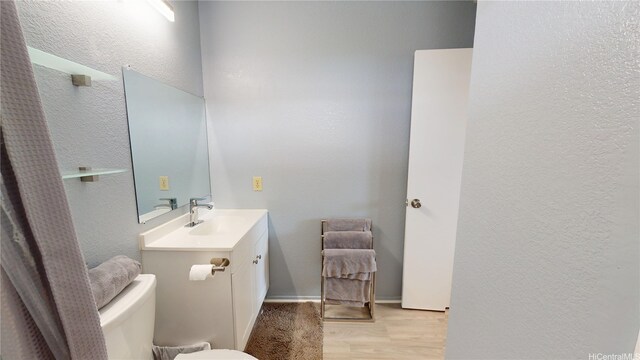 bathroom with vanity, toilet, a textured wall, and wood finished floors
