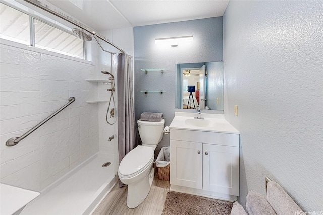 bathroom featuring toilet, a tile shower, vanity, wood finished floors, and a textured wall