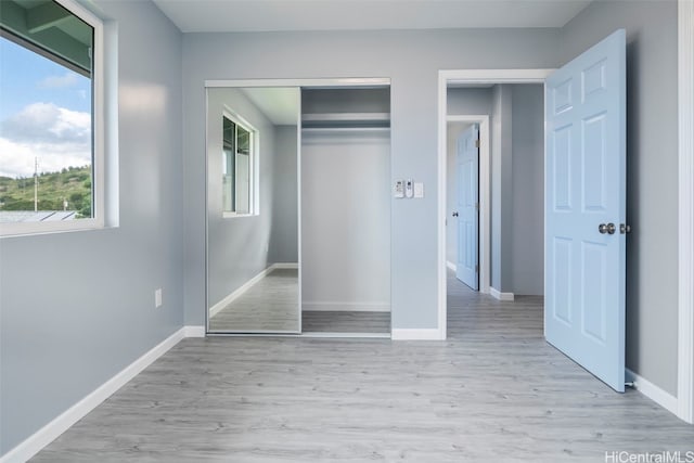 unfurnished bedroom with light wood finished floors, multiple windows, a closet, and baseboards
