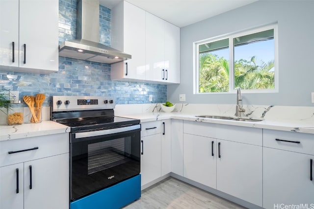 kitchen with light stone counters, a sink, wall chimney exhaust hood, stainless steel range with electric stovetop, and decorative backsplash