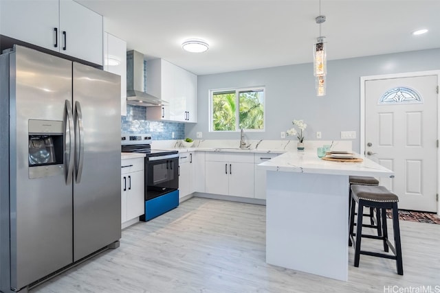kitchen featuring a peninsula, wall chimney exhaust hood, stainless steel refrigerator with ice dispenser, range with electric stovetop, and a kitchen breakfast bar