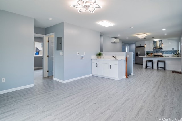 kitchen with stainless steel appliances, an AC wall unit, wall chimney range hood, light wood-style flooring, and a peninsula