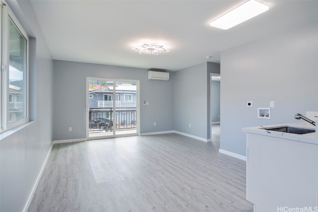 unfurnished living room featuring light wood-style flooring, a sink, baseboards, and a wall mounted AC