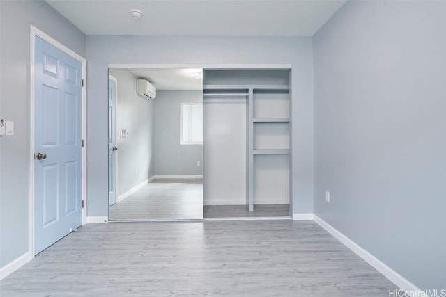 unfurnished bedroom featuring baseboards, a closet, a wall mounted AC, and wood finished floors