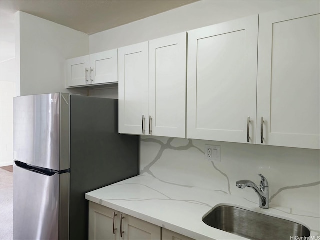 kitchen with light stone countertops, freestanding refrigerator, a sink, and white cabinets