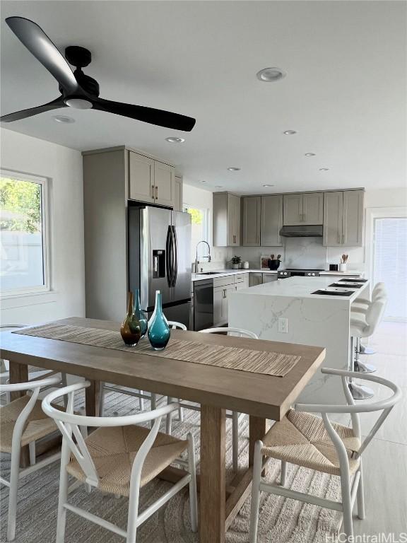 kitchen with light countertops, under cabinet range hood, a sink, stainless steel refrigerator with ice dispenser, and gray cabinets