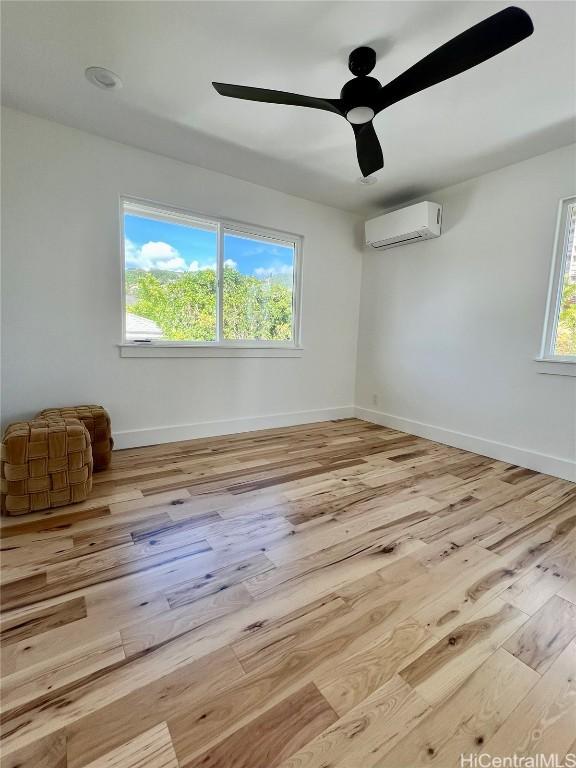 empty room with baseboards, an AC wall unit, a healthy amount of sunlight, and wood finished floors