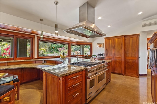 kitchen with hanging light fixtures, brown cabinetry, dark stone counters, range with two ovens, and island exhaust hood