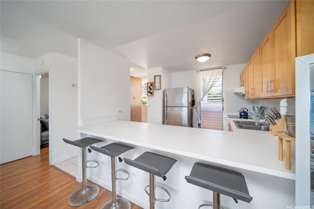3030 Ala Ilima St Unit 301, Honolulu, HI 96818 - kitchen featuring freestanding refrigerator, light countertops, light wood finished floors, a kitchen breakfast bar, and decorative backsplash