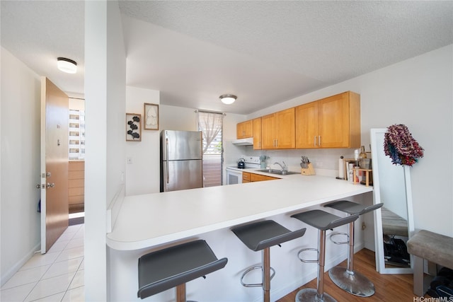 3030 Ala Ilima St Unit 301, Honolulu, HI 96818 - kitchen with freestanding refrigerator, white range with electric stovetop, under cabinet range hood, light countertops, and a breakfast bar