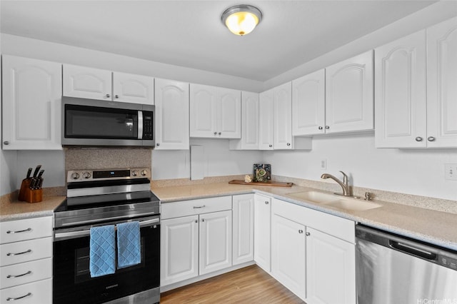 kitchen with a sink, white cabinets, light wood-type flooring, light countertops, and appliances with stainless steel finishes