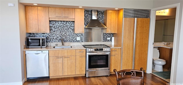 kitchen featuring a sink, wall chimney range hood, dark wood finished floors, stainless steel appliances, and decorative backsplash