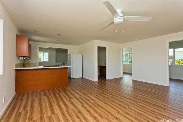 kitchen with open floor plan, a sink, freestanding refrigerator, a peninsula, and brown cabinetry