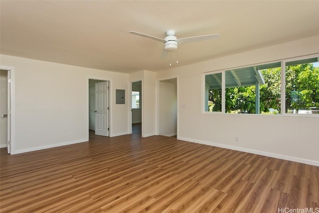 empty room with wood finished floors, baseboards, ceiling fan, and electric panel
